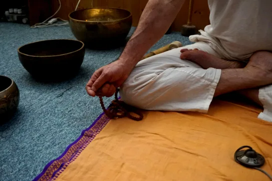Main tenant un mala, reposant sur un genou en position du lotus pendant un cours de yoga à la demande